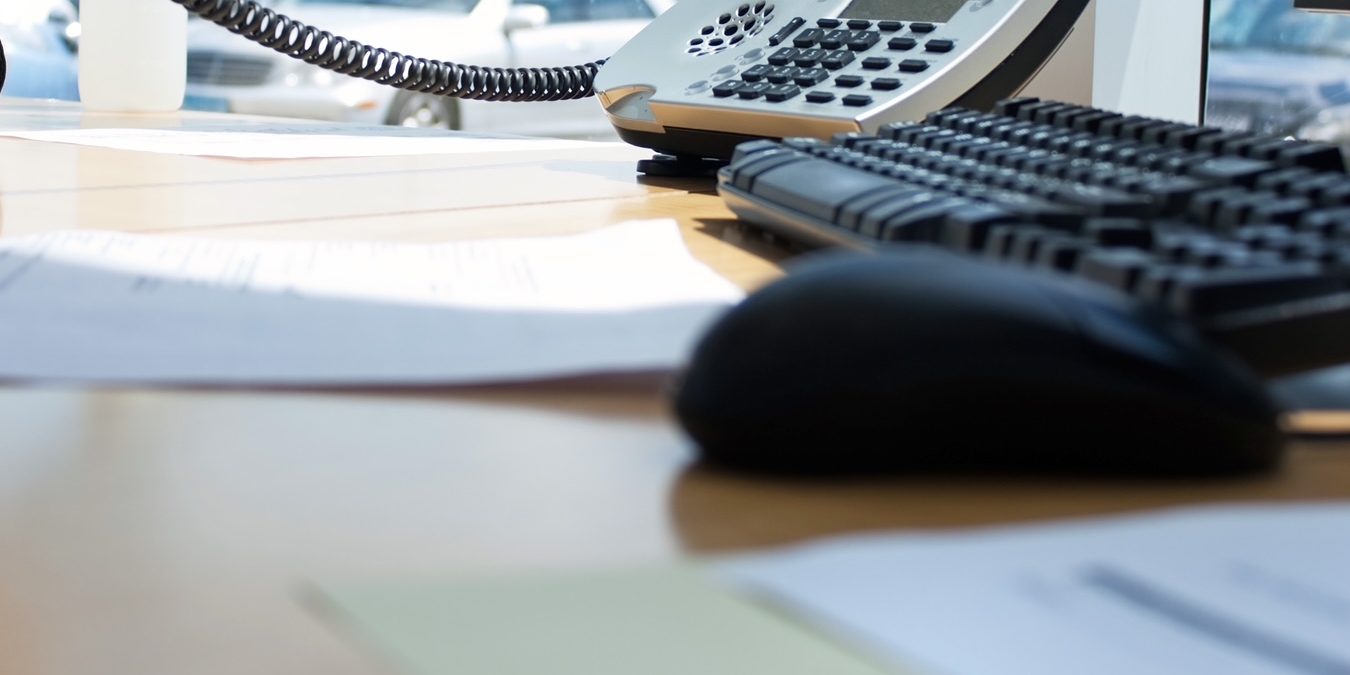 Un poste d'accueil : téléphone fixe décroché, clavier et documents posés sur le bureau.