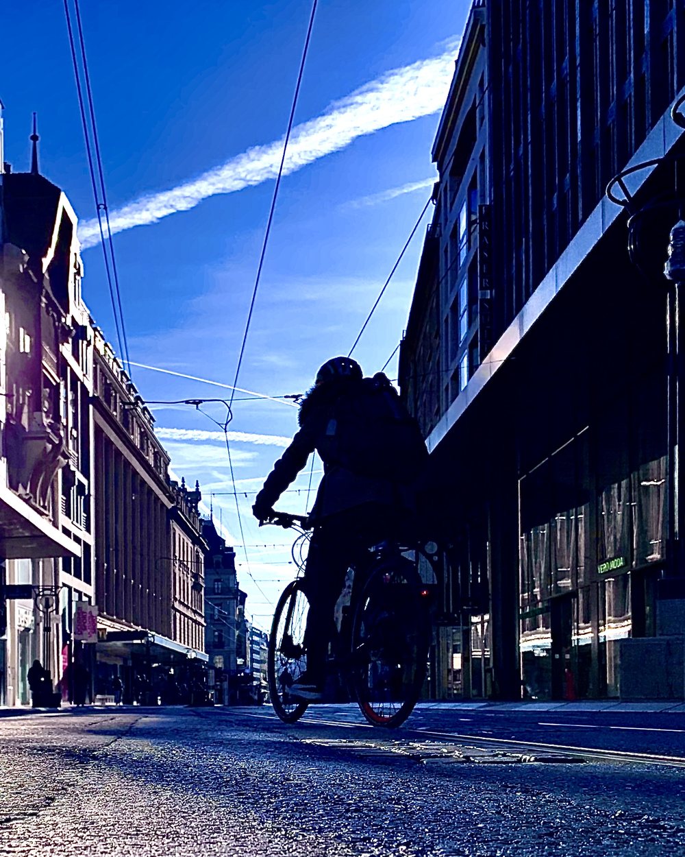 Une rue du centre de Genève au petit matin, un cycliste à contre-jour sous les lignes de tram.